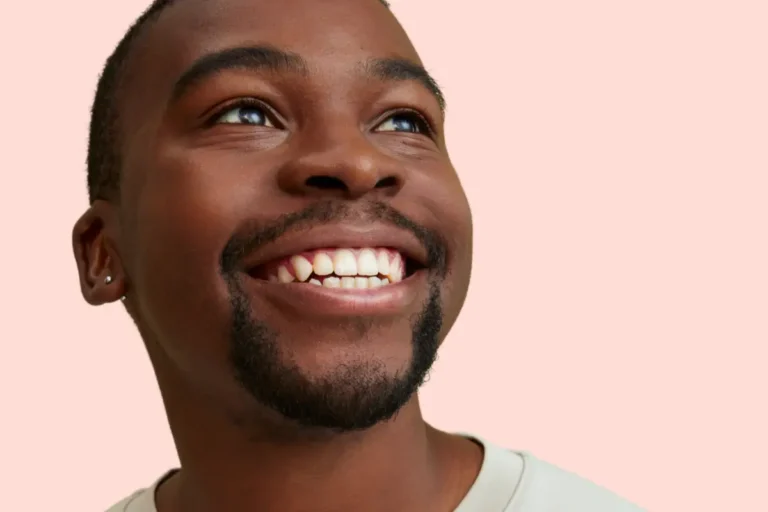 Smiling man with teeth visible against a light pink background, featured in an Urban Smile blog about bite correction in orthodontics.