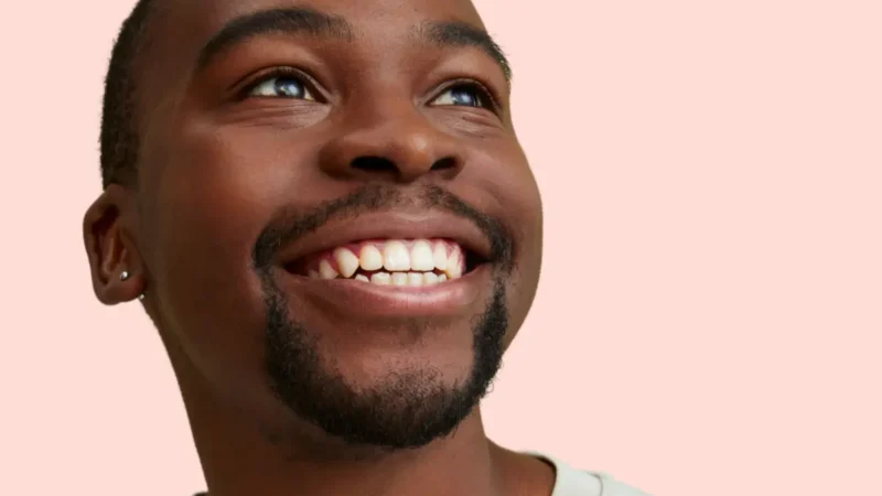 Smiling man with teeth visible against a light pink background, featured in an Urban Smile blog about bite correction in orthodontics.