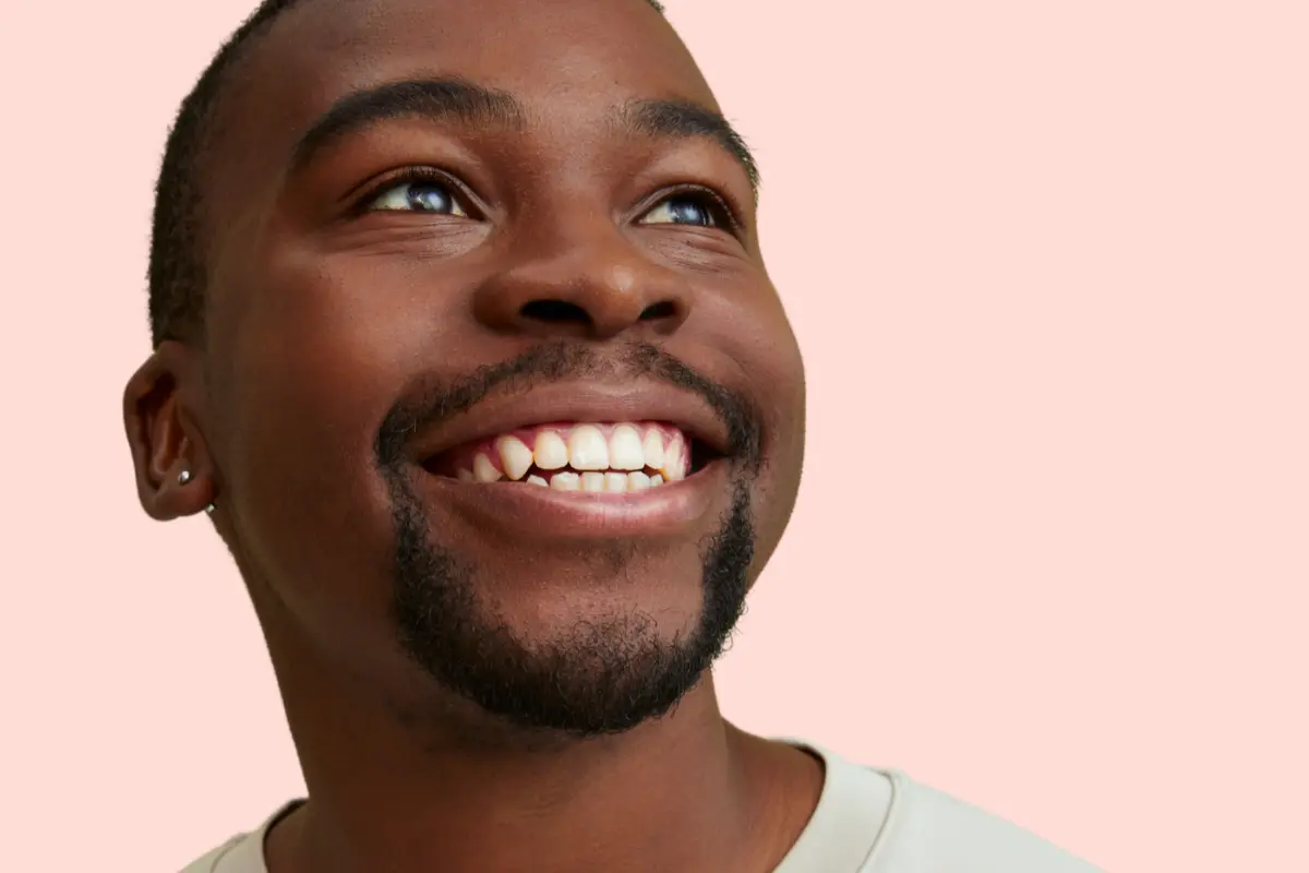 Smiling man with teeth visible against a light pink background, featured in an Urban Smile blog about bite correction in orthodontics.
