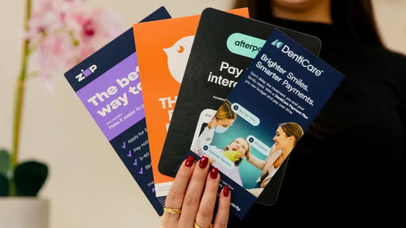 Close up of hand holding posters for clear aligner payment plan options Zip Money, Humm, Afterpay and Denticare