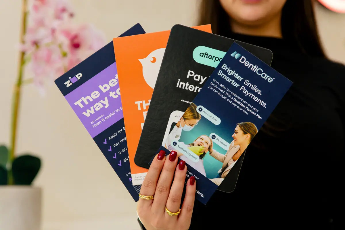 Close up of hand holding posters for clear aligner payment plan options Zip Money, Humm, Afterpay and Denticare