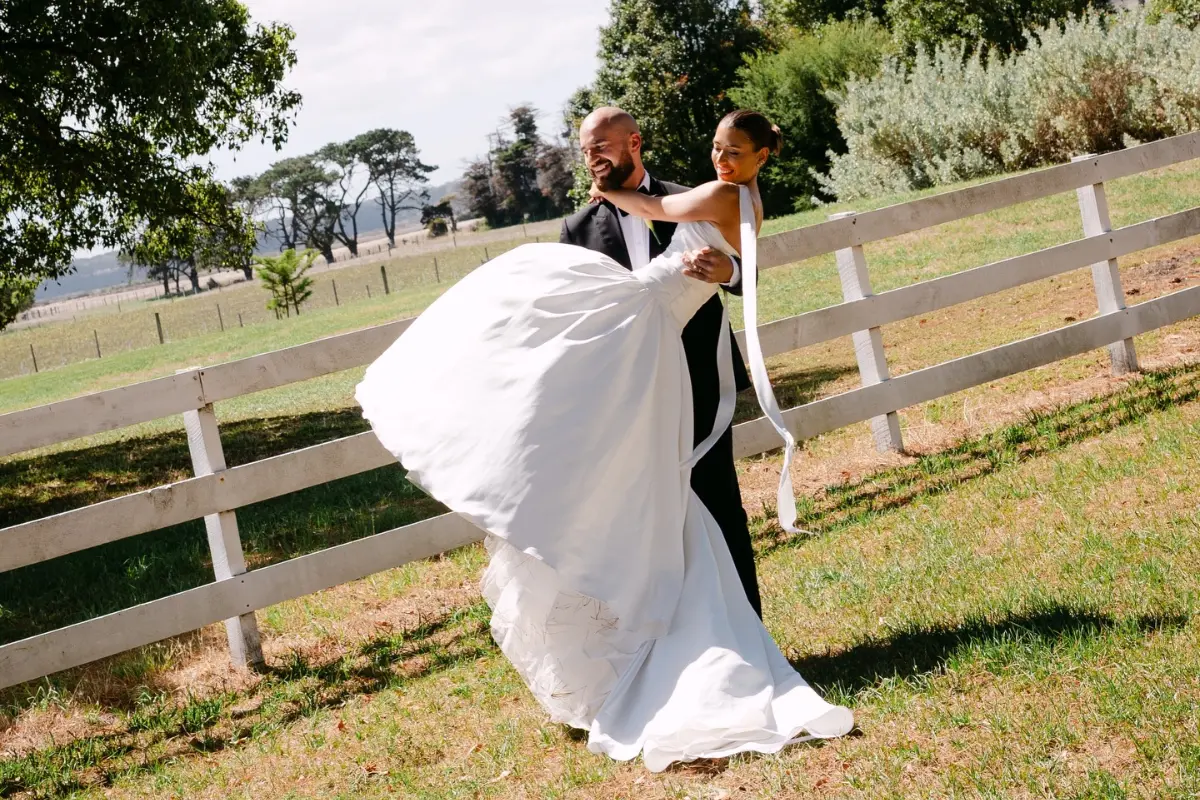 A bride showing off her wedding smile in a white wedding dress, she is held by the groom