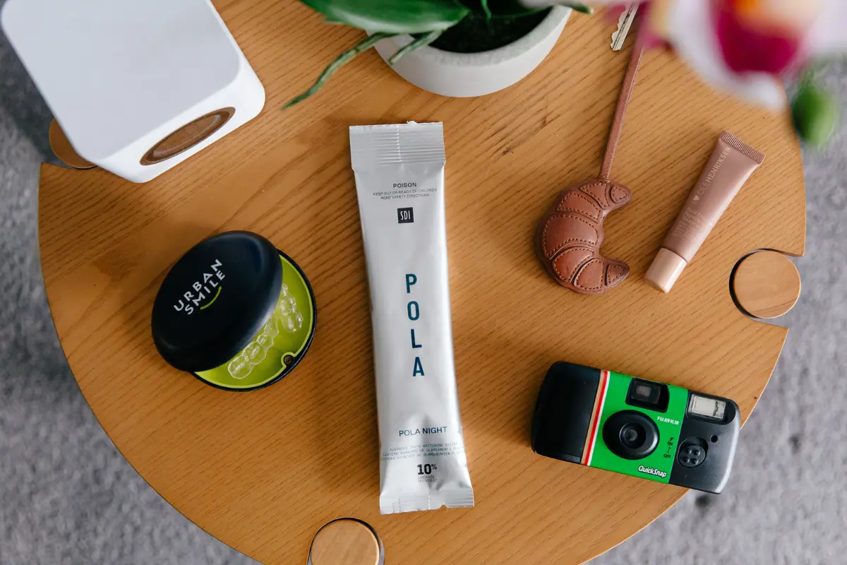 POLA Night At-Home Teeth Whitening packet on a table with Urban Smile retainer case, disposable camera, lip balm and keys