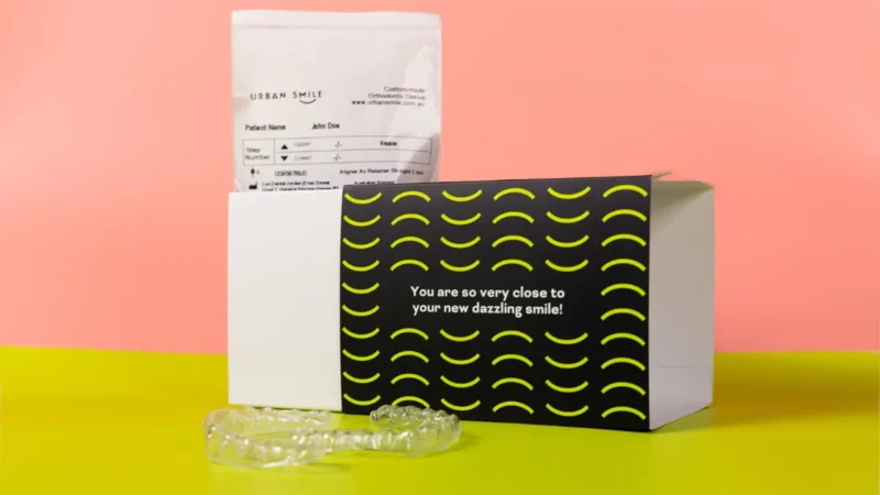 Urban Smile clear aligner box on a pink and green background with clear aligners next to it