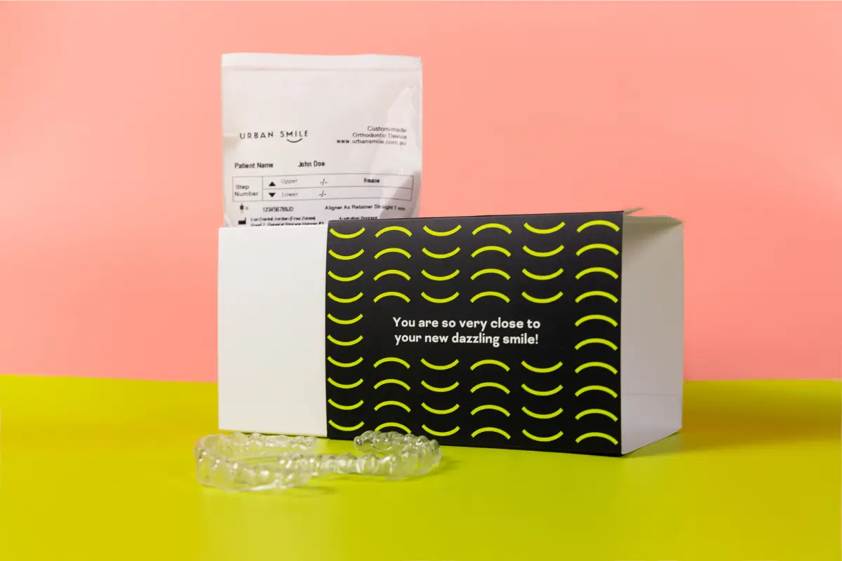 Urban Smile clear aligner box on a pink and green background with clear aligners next to it