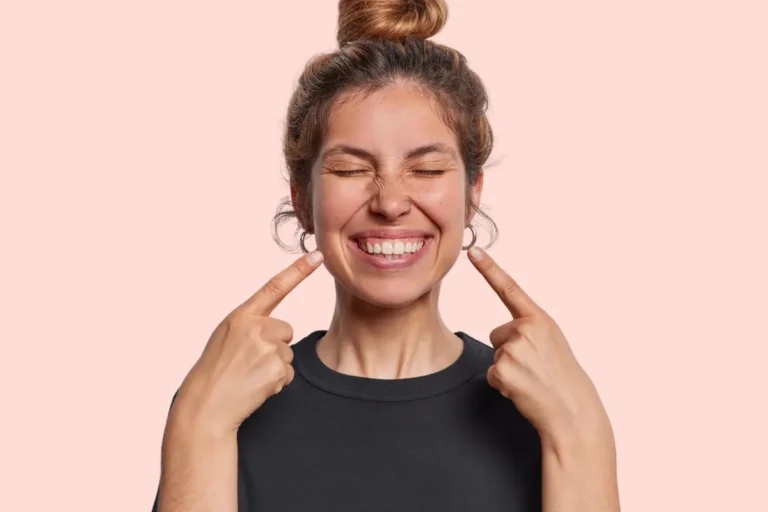 A woman pointing to her smile with both hands