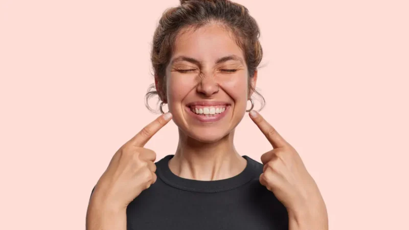 A woman pointing to her smile with both hands